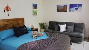 A bedroom with a bed, a grey sofa, and a potted plant. - Comfy studio on downtown, 3 blocks to ocean views, calm, safe & quiet (San Miguel de Cozumel)