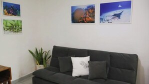 A dark grey sofa with a white pillow, a small plant, and three framed pictures on the wall. - Comfy studio on downtown, 3 blocks to ocean views, calm, safe & quiet (San Miguel de Cozumel)