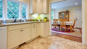 A kitchen with beige cabinets, a granite countertop, and a dining area with a wooden table and chairs. - Charming Flushing Cottage w/ Deck + Spacious Yard! (Flushing)