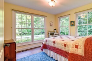 A bedroom with large windows, a bed with a quilt, a dresser, and a blue rug. - Charming Flushing Cottage w/ Deck + Spacious Yard! (Flushing)