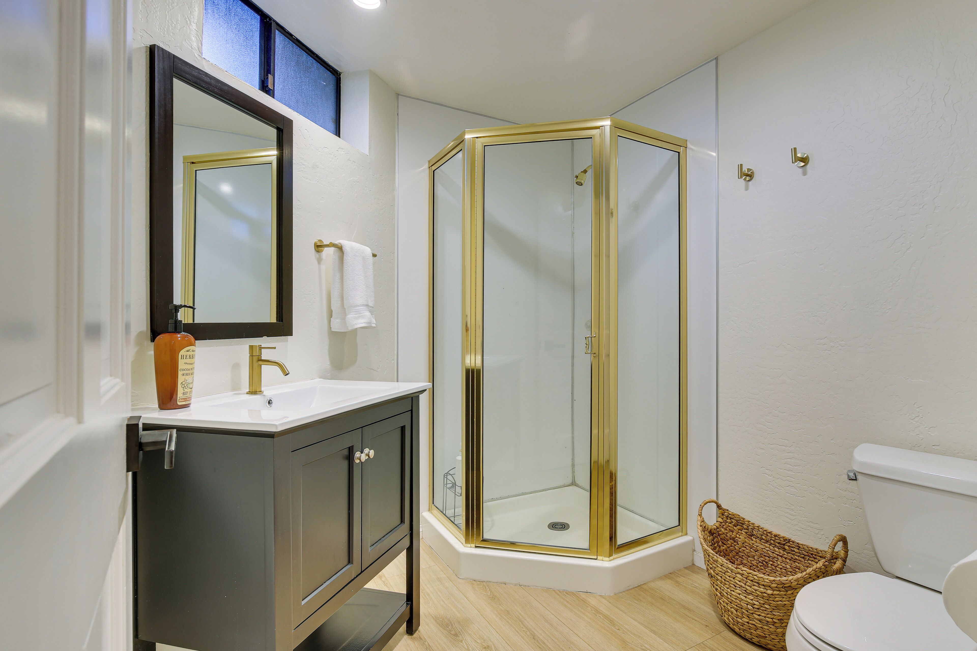 Un bagno con doccia vetrata, un lavandino bianco con rubinetto dorato e un mobile scuro.