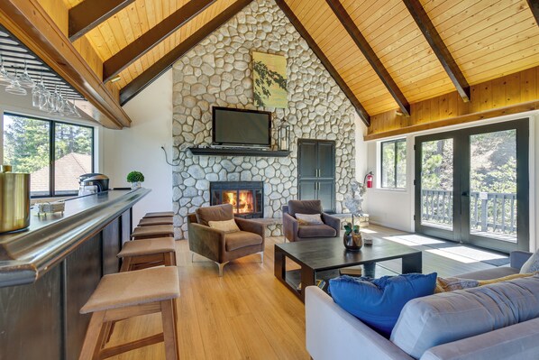 Uma sala de estar acolhedora com lareira de pedra, assentos confortáveis e uma grande janela com vista para um terraço.