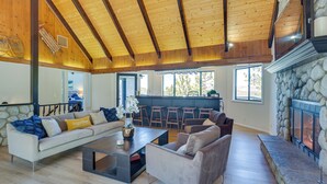 Un vaste salon doté d’un haut plafond en bois, d’une cheminée en pierre et d’une grande fenêtre offrant une vue sur l’extérieur.