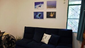 Een donkerblauwe bank met een decoratief kussen, een wandventilator en vier ingelijste kunstwerken erboven.