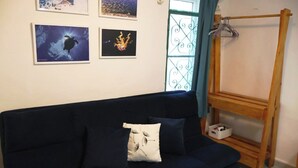 Een donkerblauwe bank met een wit kussen, een houten ezel met een witte mand, en vier ingelijste foto's aan de muur.