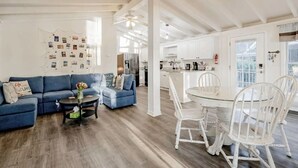 A modern living room with a blue sofa, a coffee table, and a dining area with a white table and chairs. - Lazy Creek Cove Cottage w EV Plug! (Chapin)