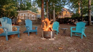 A backyard with a fire pit surrounded by four blue Adirondack chairs. - Lazy Creek Cove Cottage w EV Plug! (Chapin)