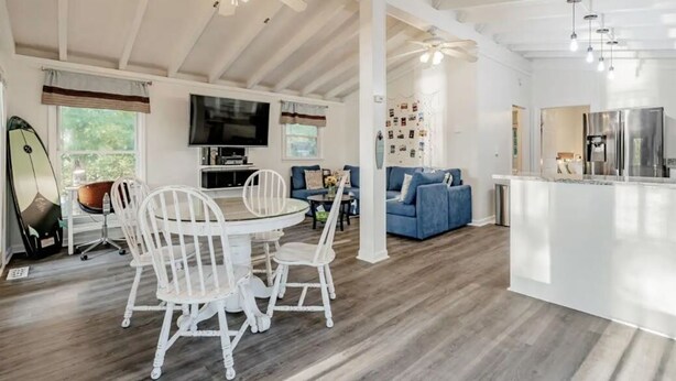 A spacious living area with a dining table, white chairs, a blue sofa, and a kitchen area with a refrigerator. - Lazy Creek Cove Cottage w EV Plug! (Chapin)
