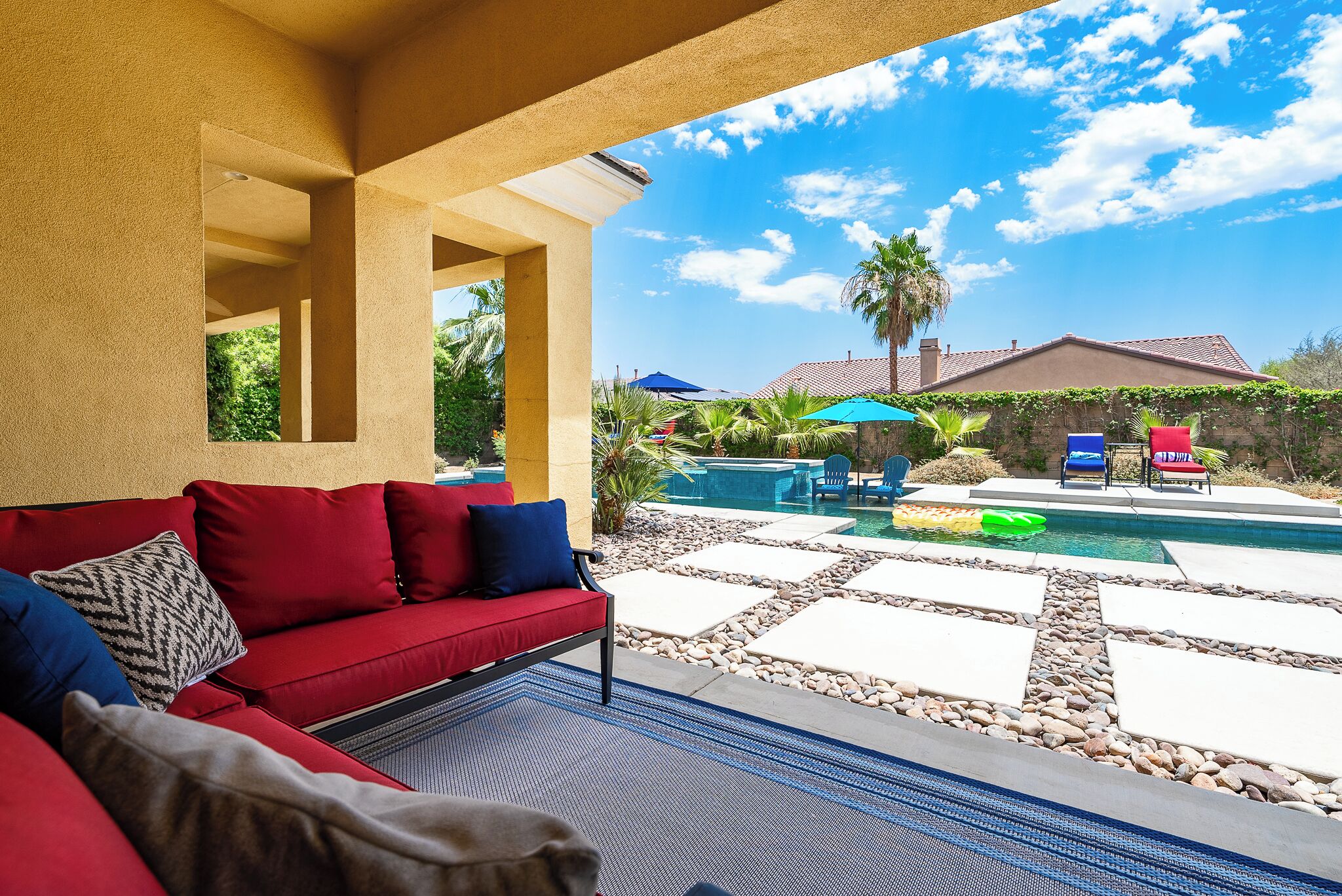 A covered outdoor area with a red sofa, a pool, and a patio with chairs and umbrellas.