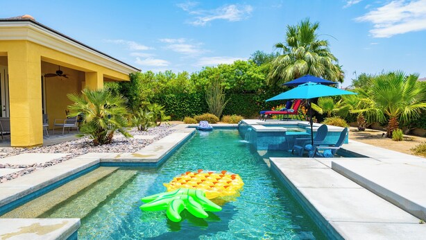 A swimming pool with clear water, surrounded by palm trees and a covered seating area. - Luxurious 5BR Resort Style Home w/ Pool & Spa (Indio)