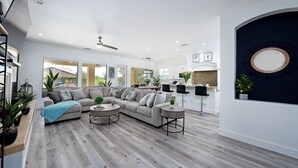 A spacious living room with a grey sectional sofa, two round coffee tables, and a large window offering a view of the outdoors. - Luxurious 5BR Resort Style Home w/ Pool & Spa (Indio)