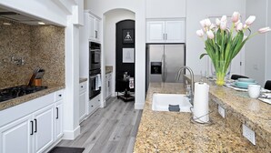 A modern kitchen with white cabinets, granite countertops, stainless steel appliances, and a vase of tulips. - Luxurious 5BR Resort Style Home w/ Pool & Spa (Indio)