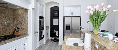 A modern kitchen with white cabinets, granite countertops, stainless steel appliances, and a vase of tulips.