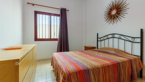 Una camera da letto con un letto, una cassettiera, un comodino, una finestra con inferriate, una tenda e un elemento decorativo al muro.
