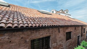 A brick building with a tiled roof and a window with metal bars.
