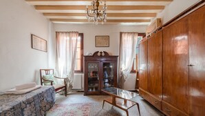 A room with a bed, a wooden wardrobe, a glass table, a wooden cabinet, and a chandelier.