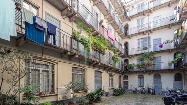 Une cour intérieure agrémentée de plantes en pot, de vélos et de linge séchant sur les balcons.