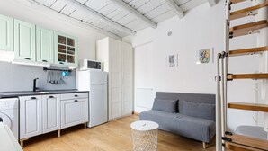Un espace de vie compact comprenant un coin cuisine, un canapé gris et une petite table ronde.