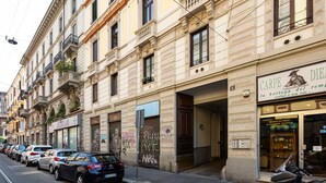 Une rue bordée de voitures garées et un immeuble dont le rez-de-chaussée abrite un commerce.