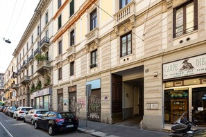 Une rue bordée de voitures garées et un immeuble dont le rez-de-chaussée abrite un commerce.