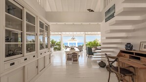 A spacious room with a large open-plan layout, featuring a dining area with a view of the ocean, a seating area with a pergola, and a wooden sideboard with decorative items. - The Beach House - Coral Estate Resort (Sint Willibrordus)