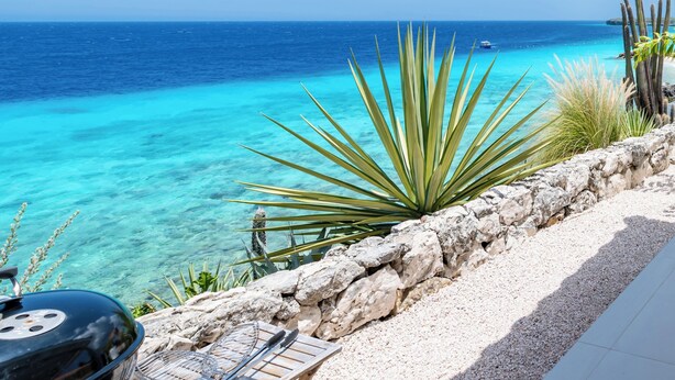 A patio with a view of the ocean, a grill, and a stone wall. - The Beach House - Coral Estate Resort (Sint Willibrordus)