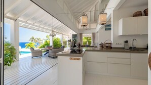A modern kitchen with a view of the ocean, a dining area with wicker furniture, and a poolside setting. - The Beach House - Coral Estate Resort (Sint Willibrordus)