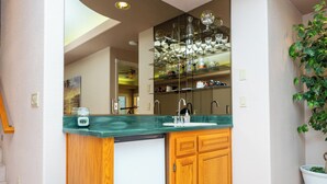 A bathroom with a green countertop, wooden cabinets, a glass shelf with decorative items, and a potted plant. - Bullhead City Riverfront Home with Dock! (Bullhead City)