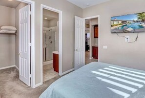 A bedroom with a bed, a TV mounted on the wall, and a door leading to a bathroom. - Lux Desert Oasis w/ saltwater pool near Coachella (Indio)