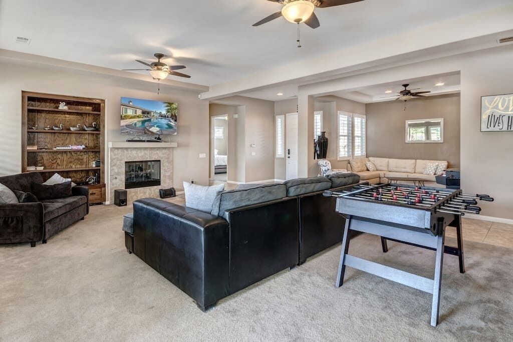 A spacious living room with a foosball table, a large sectional sofa, a fireplace, and ceiling fans.