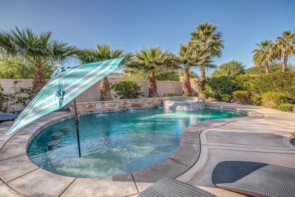 A swimming pool with a curved design, surrounded by palm trees and a stone wall. - Lux Desert Oasis w/ saltwater pool near Coachella (Indio)