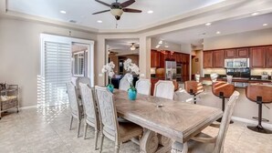 A spacious dining area with a large wooden table and chairs, a ceiling fan, and a view into the kitchen area. - Lux Desert Oasis w/ saltwater pool near Coachella (Indio)