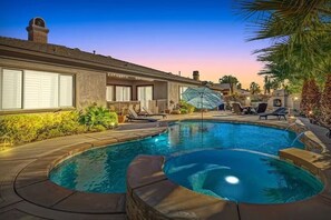 Une piscine avec un jacuzzi, des chaises longues et des parasols.