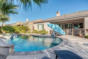 A swimming pool with a curved edge, surrounded by a patio area with a lounge chair and umbrella. - Lux Desert Oasis w/ saltwater pool near Coachella (Indio)