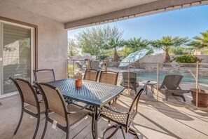 A covered patio with a table and chairs, overlooking a swimming pool and palm trees. - Lux Desert Oasis w/ saltwater pool near Coachella (Indio)