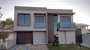 Une maison moderne à deux étages, dotée d’un grand garage, d’un petit jardin devant avec des plantes en pot et d’une allée pavée.