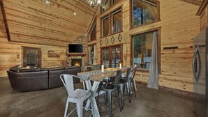 A wooden cabin interior with a dining table, chairs, a sofa, and a fireplace.