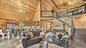 A spacious living area with a large brown leather sofa, a coffee table with decorative items, and a wooden staircase leading to an upper level.