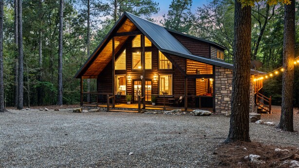 A log cabin with a stone foundation, large windows, and a porch with outdoor seating.
