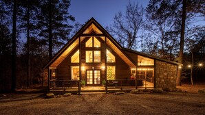 A log cabin with a large front porch, stone foundation, and a Christmas tree.