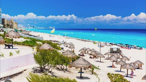 Una spiaggia con ombrelloni di paglia, una torretta per i bagnini e un cielo azzurro intenso.