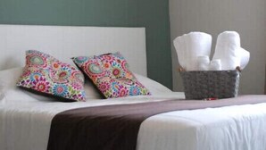 Una camera d'albergo con un letto, cuscini colorati, un cesto di asciugamani e un condizionatore d'aria a parete.