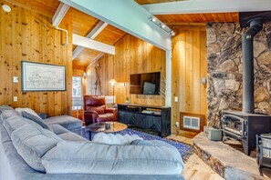Un salon chaleureux avec un mur en pierre, un plafond en bois, une cheminée, un canapé, un téléviseur et un fauteuil en cuir.