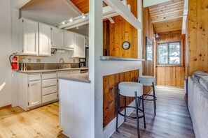 Une cuisine avec des meubles blancs, un îlot central en bois et un coin bar avec des tabourets.