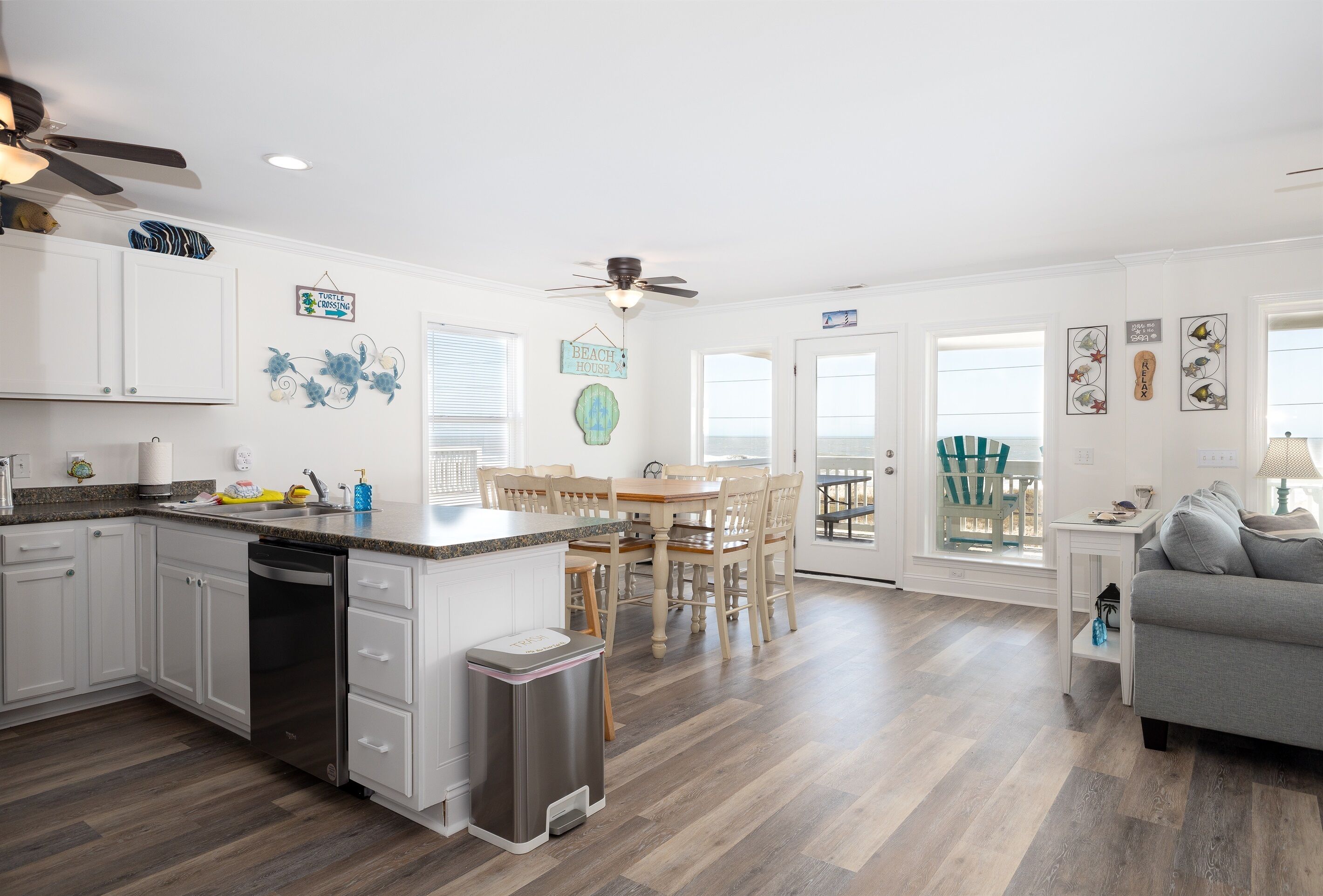 A modern kitchen with white cabinets, a wooden dining table, and a ceiling fan.
