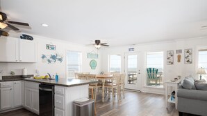 A modern kitchen with white cabinets, a wooden dining table, and a ceiling fan. - Unobstructed Views and Beach at "Turtle Time!" (North Topsail Beach)
