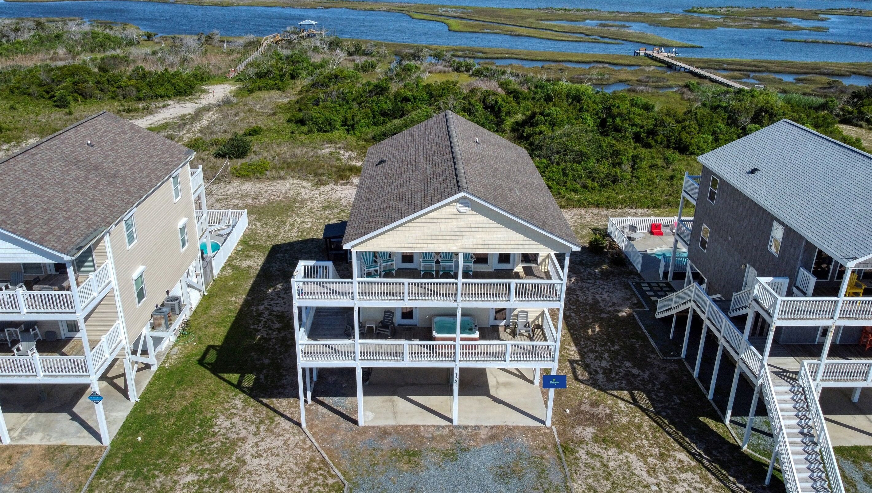 A beachfront property with a two-story house featuring a balcony with outdoor seating and a hot tub.