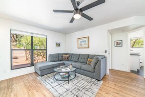 Un salon moderne avec un canapé d’angle gris, une table basse en verre et un ventilateur de plafond.