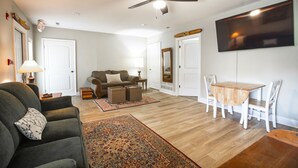Ein Wohnzimmer mit Sofa, Couchtisch, Esstisch mit Stühlen, Deckenventilator und flach an der Wand befestigtem Flachbildfernseher.