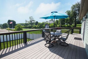 A wooden deck with a table and chairs, an umbrella, and a signboard. - Welcome to The Captain and Crew Quarters on Anchor Drive at Apple Valley Lake! (Howard)